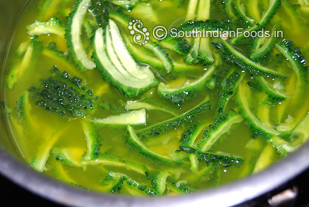 in a bowl add water salt turmeric powder lemon juice and thinly sliced bitter gourd mix well leave it for 5 min